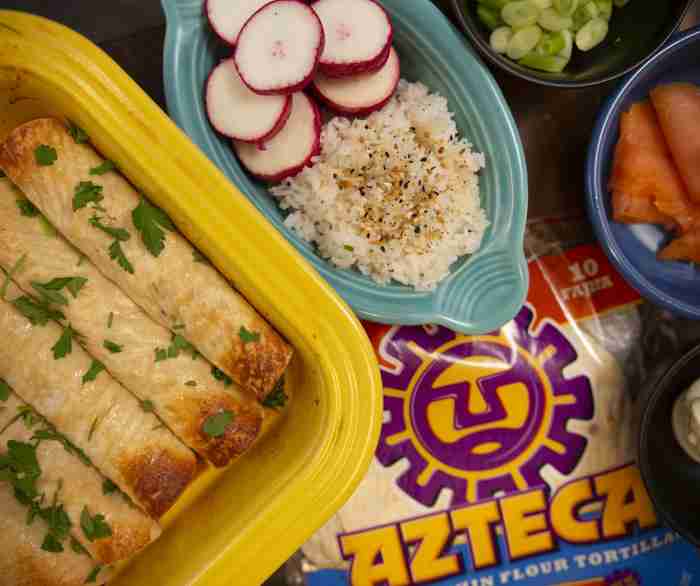 A yellow serving dish filled with Azteca's Salmon Taquitos next to a bowl of rice that is on top of a package of Azteca Flour Tortillas.