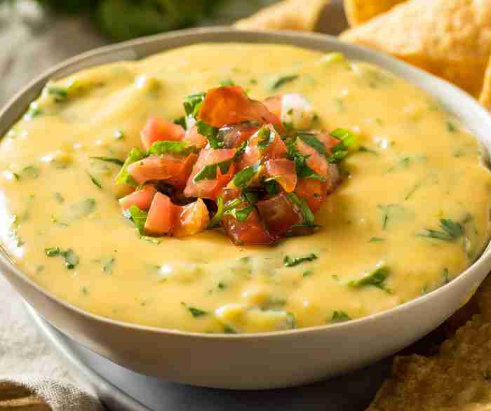 A bowl of Spicy queso dip with a scoop of pico de gallo on top.