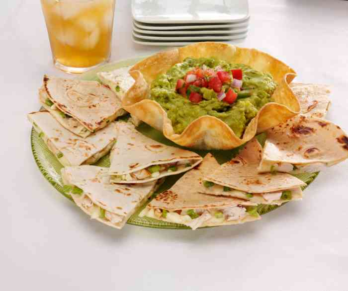 Some Grilled chicken quesadilla wedges around an Azteca salad shell filled with Guacamole.