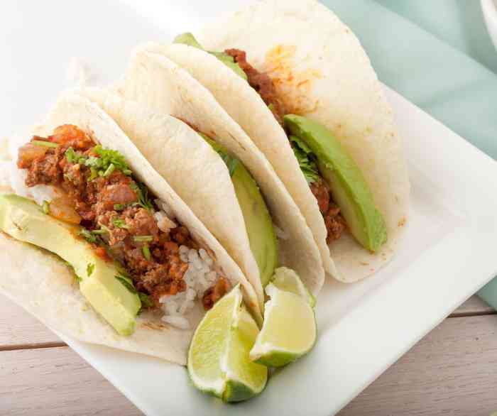 Three Korean BBQ beef tacos on a white plate with a few lime wedges.