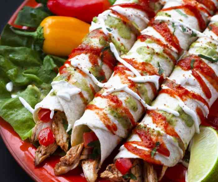 Three Spicy Beef Fajitas rolled tightly and covered with crema, red and green salsa, and on a bed of lettuce and peppers.