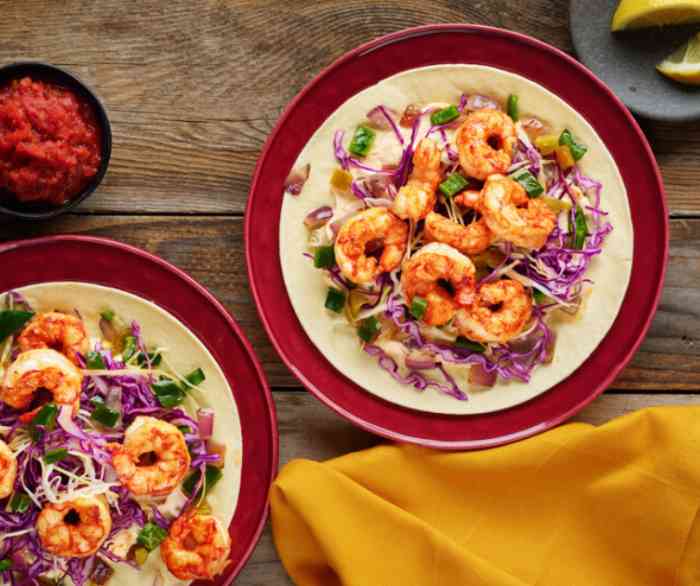 Two Ensenada Shrimp Tacos on red plates atop a wooden table.