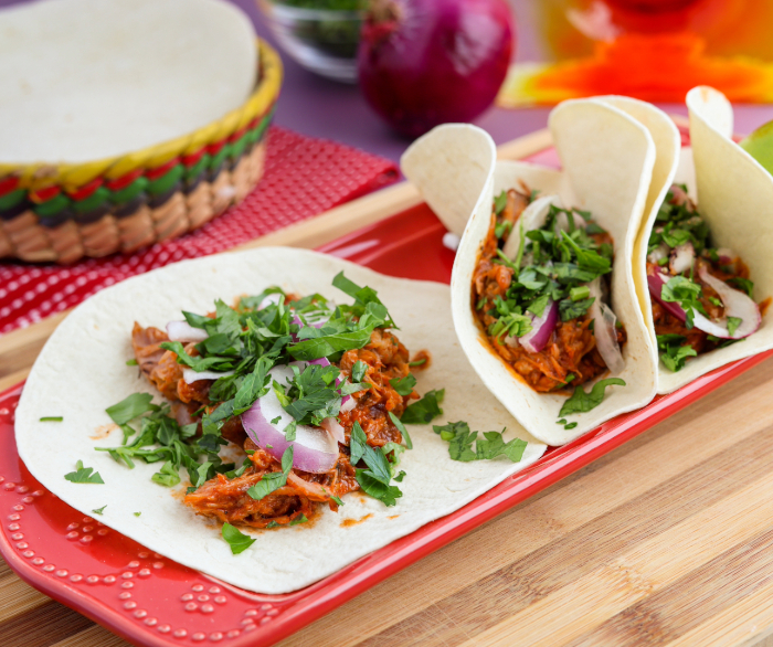 One open-faced and two rolled Miami Pork Tacos on a rectangular red plate.