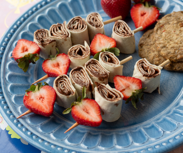 Some Nutella wrap skewers and strawberries on the skewers on a blue plate.